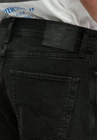 Jeans negre din denim cu o eticheta din piele la spate, având o croială clasică și detalii de cusătură subtile pe buzunare.