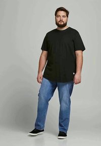 Black cotton t-shirt with short sleeves, crew neck, and a straight fit, paired with blue denim jeans and black sneakers.