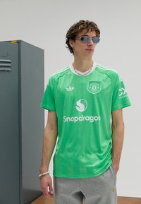Zöld focimez fehér szegéllyel, középen logóval és "Snapdragon" felirattal. Szürke edzőnadrággal és napszemüveggel viselve.