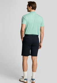 Mintgrøn kortærmet polo, mørkeblå shorts, hvide sokker og casual sko med blå accenter. Glat tekstur og klassisk pasform.
