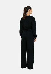 Bluză neagră cu umeri căzuți, manșete ribelizate și pantalonii largi asortați. Textură moale, croială casual și design minimalist.