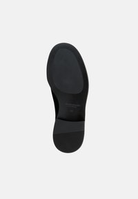 Μαύρη σόλα παπουτσιού με ομαλή επιφάνεια, στρογγυλεμένο σχήμα και υφή αντιολισθητικού καουτσούκ στη φτέρνα. Ορατές ενδείξεις για τη μάρκα και το μέγεθος.