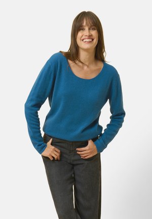 Blauer Rundhalsausschnitt-Pullover aus weichem, strukturiertem Stoff, kombiniert mit dunklen, hochgeschnittenen Jeans. Der Pullover hat lange Ärmel und einen lässigen Schnitt.