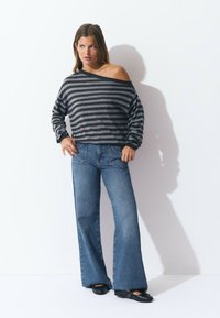 Suéter de rayas grises y negras con los hombros al descubierto, combinado con unos jeans de tiro alto de campana azules y planos negros con detalles de tachuelas.