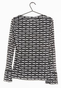 Blouse noire à manches longues avec un motif répété de léopards blancs. Le tissu semble léger avec une texture légèrement transparente ; poignets froncés.