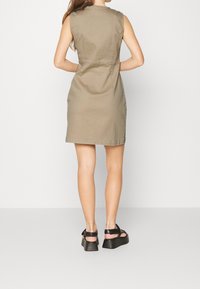 Khaki mekko ilman hihoja, jossa on istuva yläosa, suora leikkaus ja hienovaraiset ompelutiedot, yhdistetty mustiin platform-sandaaleihin.