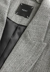 Blazer gris en chevron avec col structuré, doublure en satin noir et étiquette "NEXT" cousue à l'intérieur du col.