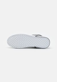 Suela de zapatilla blanca con un patrón geométrico texturizado. Detalles en negro en la parte superior. Diseño plano adecuado para uso casual.