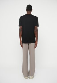 Camiseta de algodão preta com um corte descontraído, combinada com calças largas cinza claro e ténis brancos, vista de costas contra um fundo branco.