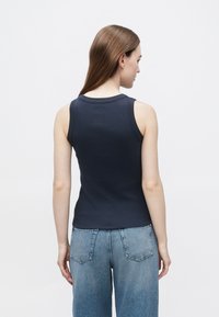 Granatowy top bez rękawów o dopasowanym kroju, z prążkowaną fakturą i okrągłym dekoltem, zestawiony z jasnoniebieskimi dżinsami z tylnymi kieszeniami.