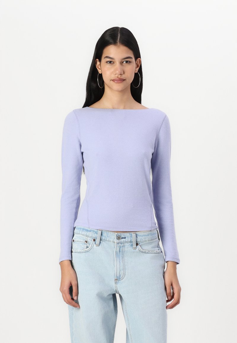 Light purple long-sleeve top with a boat neckline, made of soft material, paired with light blue high-waisted jeans, featuring front pockets.
