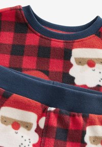 Rot-schwarz kariertes Fleece-Gewebe mit einem marineblauen Rippenkragen. Enthält Weihnachtsmann-Gesichter; weiche Textur und festliches Design.