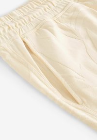 Pantaloni jogger de culoare crem, cu un design texturat, talie elastică și buzunare laterale, confecționați dintr-un material tricotat moale.