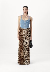 Top din denim cu fermoar, asortat cu o fustă maxi cu imprimeu de leopard în tonuri bej și maro. Modelul ține o geantă de mână neagră.