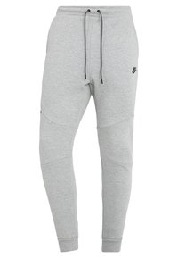 Šedé tepláky Nike s elastickým pasem na stažení, zúženými nohavicemi a kontrastními panely na kolenou. Vyrobeny z měkké, texturované látky s logem jako ozdobou.