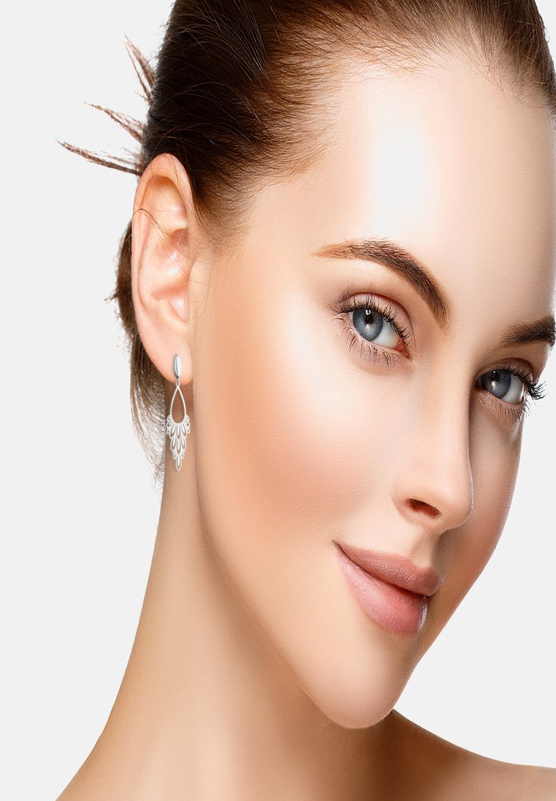 Orecchini a goccia argentati con un intricato design a filigrana appesi a un semplice perno, che completano un incarnato chiaro e levigato e un trucco leggero.