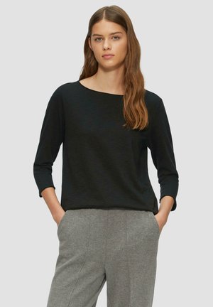 Haut noir à manches longues avec un décolleté évasé, fabriqué à partir d'un matériau léger. Présente une coupe décontractée et de légentes fentes sur les côtés.