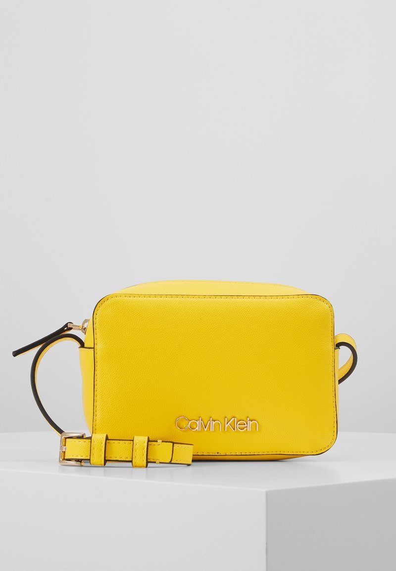 Borsa a tracolla in pelle gialla di forma rettangolare, con il marchio "Calvin Klein" in oro, dotata di tracolla removibile e superficie testurizzata.