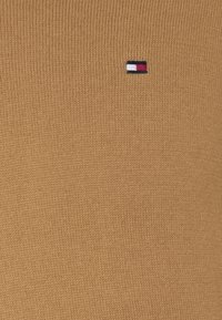 Ruisutettu ruskea neulepusero. Sisältää pienen logon punaisena, valkoisena ja sinisenä. Yksinkertainen muotoilu ja tasainen väri.