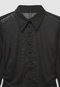 Blusa nera trasparente con colletto classico, sette bottoni neri sul davanti e tessuto leggermente zigrinato con una finitura liscia.