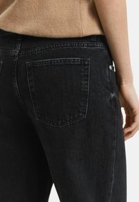 Jeans en denim noir avec une texture légèrement usée. Comprend deux poches arrière, des coutures contrastantes et une taille mi-haute.