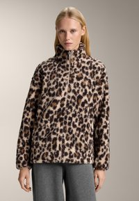 Giacca in pile con stampa leopardata, colletto alto, chiusura a zip e texture morbida, caratterizzata da macchie marroni e nere su uno sfondo beige chiaro.