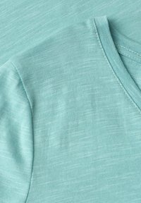 Tissu vert menthe doux avec de fines stries blanches horizontales, montrant les coutures détaillées d'un col plié et d'une couture d'épaule.