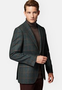 Ciemnozielona marynarka w kratę z brązowymi akcentami, wykonana z teksturowanej tkaniny. Posiada klapy w stylu notch, dwa guziki i kieszenie boczne.