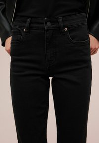 Zwarte denim jeans met een slim fit ontwerp, voorzien van een knoopsluiting, vijf zakken en subtiele stikseldetails op de tailleband.