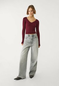 Top long-sleeve côtelé bordeaux avec un col festonné, associé à un jean large gris clair et des escarpins noirs à bouts pointus ornés de clous.