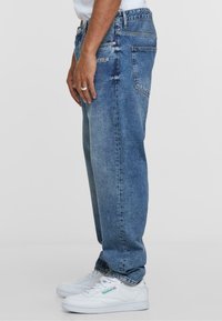 Jeans in denim azzurro chiaro con vestibilità comoda e cuciture visibili, caratterizzati da un sottile logo sulla tasca posteriore e una texture vissuta.