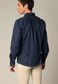 Navyblauwe button-up shirt van katoen, met een klassieke kraag, lange mouwen en een gladde textuur. Zichtbare achternaaddetail.