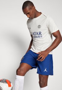 Hvid sportsjersey med subtile mønstre, prydet med blå "QATAR AIRWAYS" tekst og logo. Sammen med blå sportsbukser og hvide sokker.