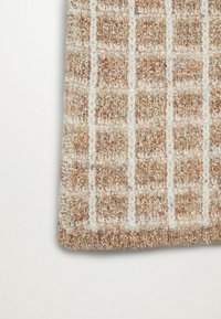 Tejido de punto en tonos beige y crema con un patrón de cuadros. La textura parece difusa con una superficie suave y táctil. Los bordes están finamente acabados.