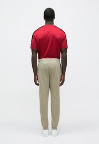 Piros rövid ujjú póló fekete oldalsávokkal, világos bézs színű melegítőnadrággal, rugalmas derékpánttal, és fehér tornacipővel.