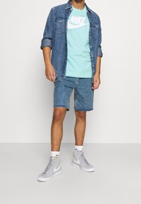 Koszula dżinsowa nałożona na jasnoniebieski t-shirt Nike. Niebieskie szorty dżinsowe i szare sneakersy z białymi akcentami dopełniają stylizację.