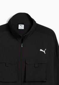 Chaqueta negra con un alto cuello, con cremallera completa y dos bolsillos frontales, adornada con un logo blanco de Puma en el lado izquierdo del pecho.