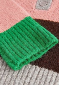 Gros plan sur une manche de pull de couleur multicolore avec un poignet côtelé vert et des sections tricotées contrastées en rose, marron et beige, agrémentées d'un bouton.