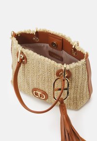 Kudottu beige laukku ruskeilla nahkaosilla, kultaisilla yksityiskohdilla ja tupsulla. Ominaisuuksiin kuuluu teksturoitu pinta ja pyöreä muoto, jossa on tilava sisus.