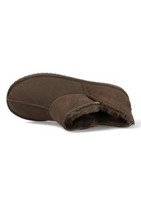 Bruine suede pantoffel met een zachte, met bont gevoerde binnenkant, gestikte accenten en een ronde neus, met een platte, gestructureerde zool voor grip.