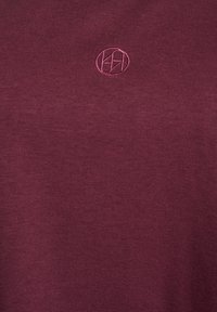 Bordeaux t-shirt met een gladde textuur, voorzien van een klein geborduurd cirkelvormig logo in een bijpassende kleur op de borst.