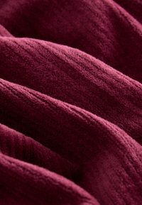 Gros plan d'un tissu bordeaux doux et côtelé avec une texture visible et des plis créant un motif ondulé.