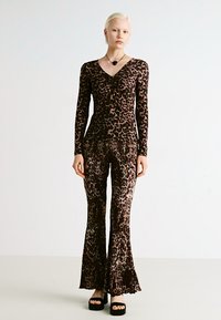 Leopard print bodysuit and flared pants made of soft, textured fabric. Color palette includes browns and tans, with long sleeves and v-neckline.
