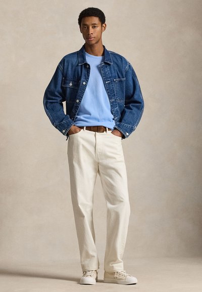 Geacă din denim, pulover cu guler rotund în albastru deschis, pantaloni crema și teniși albi. Detalii includ nasturi și o curea maro.