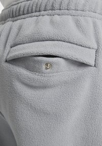 Los pantalones de chándal de felpa gris claro cuentan con un bolsillo trasero con cierre a presión y una tela texturizada, que exhibe una apariencia suave y cepillada.