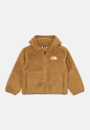Ruda pūkuota zip-up gobtuvu striukė su "The North Face" logotipu kairėje krūtinės pusėje ir dviem priekiniais kišenėmis, padėta ant baltos fono.
