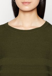 Maglione a maglia verde oliva con collo a girocollo rigato e texture liscia, che mette in risalto linee orizzontali e una silhouette aderente.