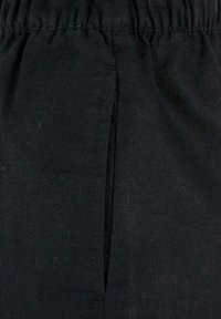 Gros plan sur un short en tissu noir avec une taille élastique et une couture verticale sur la poche latérale.