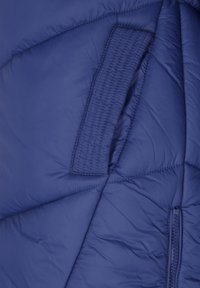 Blåt quiltet jakke stof med en syet rektangulær lap og en delvist synlig lynlås på højre side.