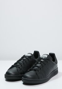 Svarta lädersneakers med perforerade sidopaneler, runda snören och gummisulor. Märkesdetaljer finns på tungan och hälen.